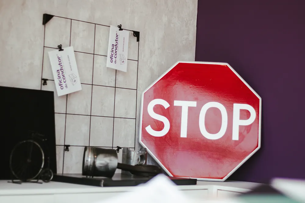 Placa de STOP encostada a uma parede roxa, ao lado de uma grelha com cartões da Oficina do Condutor